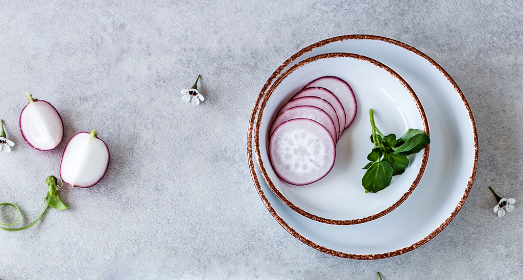 Dishes from the Coral Brown collection in porcelain, with a brown border, served with radishes and herbs