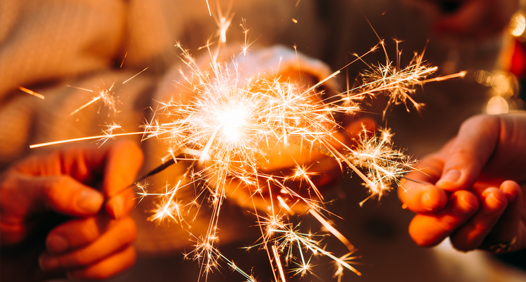 3 mãos a segurar velas sparklers acesas - imagem ilustrativa do artigo “Tradições de passagem de ano à volta do mundo”